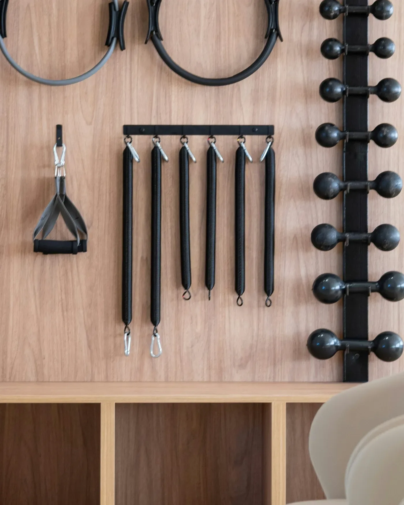 A wooden wall rack with small dumbbells, resistance cables and pilates rings — illustrating strength